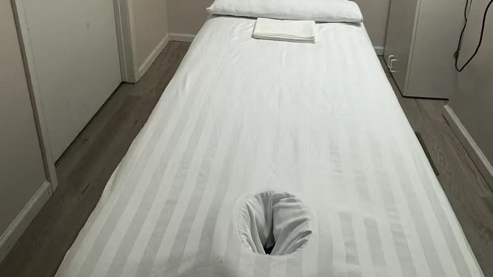 White-linen massage table and folded towels in a Jin’s Massage treatment room