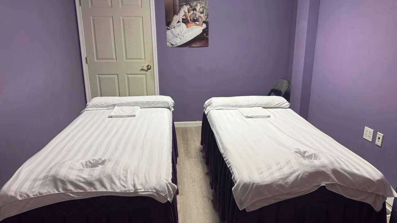 Two massage tables with white linens side by side in the purple-walled treatment room at Jin’s Massage in Glenside