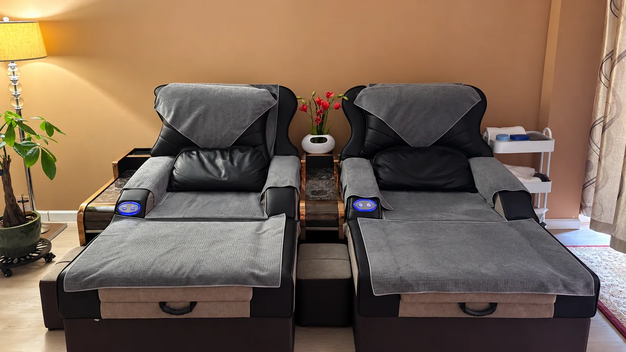 Two foot massage recliners with gray covers beside a warm lamp at Jin’s Massage in Glenside