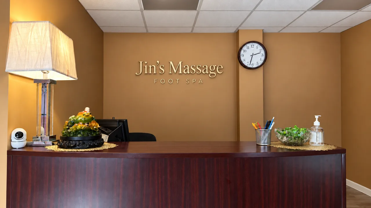 Wooden reception desk with a warm lamp and wall clock at Jin’s Massage in Glenside