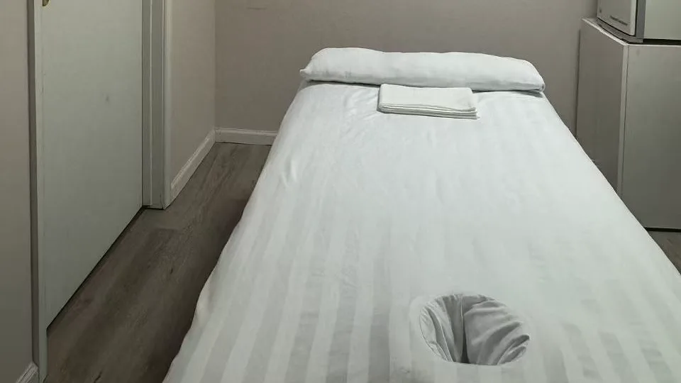 White-linen massage table with a face opening and folded towels in a Jin’s Massage treatment room